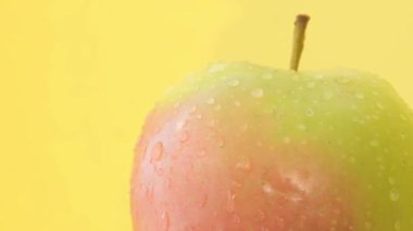 Macro video of a large apple in water drops rotating on a yellow background. Close up
