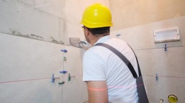 Laying ceramic tiles on the wall using tools and adhesive mixtures. Worker repairman man builder craftsman installs ceramic tiles
