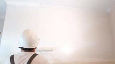 The worker paints the wall white. Painting the walls with acrylic paint. Repair in the apartment