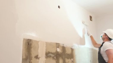 A man paints a wall white. The man is making repairs in the room. Modern interior in the house. Home renovation concept