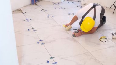 Professional laying of ceramic tiles on a concrete floor. The worker is dressed in overalls and a construction helmet, making repairs in the house