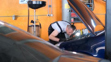 Changing the oil in a car at a car service station. The mechanic inspects the car engine.