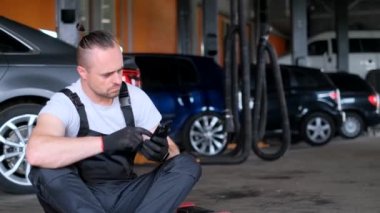 Auto mechanic uses a smartphone, he sits and rests from work. Car service.