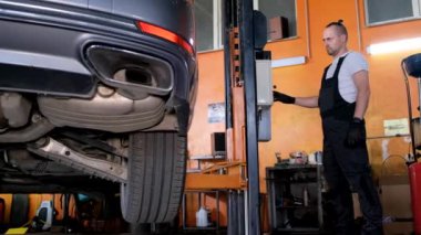 A car mechanic diagnoses the cars undercarriage. Raised car at repair station. Car service station