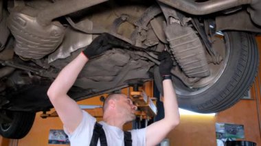 A car mechanic diagnoses the cars undercarriage. Raised car at repair station. Car service station