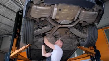 A male mechanic in a garage is repairing a car on a ramp. Car chassis repair. The work of a car mechanic