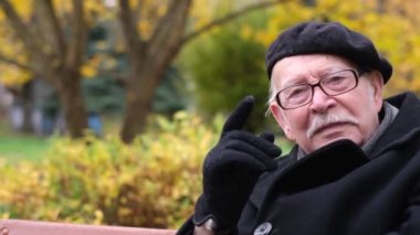 A wise old senior sits on a bench in an autumn park and says something. Seniors. Age