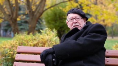 A wise old senior sits on a bench in an autumn park and says something. Seniors. Age