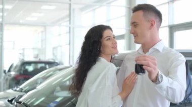 Happy married couple owners of a new car. They are in a car dealership and show the keys. Car business concept