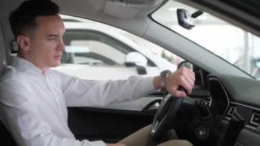 Young business man stroking the steering wheel in an electric car. Buying a new car at a dealership.