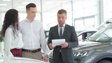 A lovely couple is talking to a manager while buying a car at a car dealership. Car dealership.