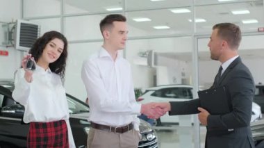 A car dealer consults a young couple in a car dealership. Professional employee helping with the selection of a new car, talking and gesturing. 4k video