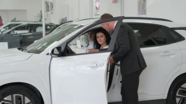 A happy young family buys a luxury car. Car sales manager showing a new car. Car sales concept.