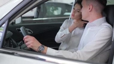 A beautiful European woman is buying a new car with her husband in a car dealership. They inspect the new car interior