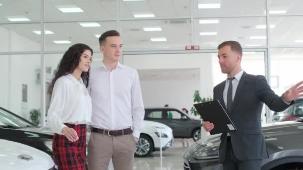 Young Couple Talking Sales Consultant Car Shop Telling Them Car — 图库视频影像