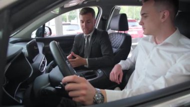 A salesperson at a car dealership shows a customer the interior of a new car in the US. New car dealership