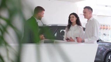 A married couple signs an order for the purchase of a car at a car dealership. A car salesman is talking to a couple about buying a new car.