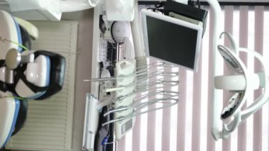 Rahat bir sandalye, ekran ve aletlerle donatılmış modern bir diş hekiminin dikey videosu. Beyaz dişçi sandalyesi.