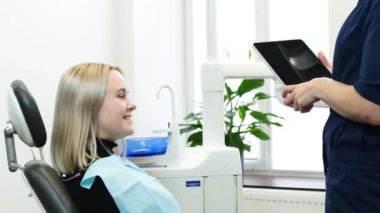 Modern bir ofiste dişçi randevusunda pozitif sarışın. Kadın bir dişçi, tablet kullanan bir hastaya danışır..