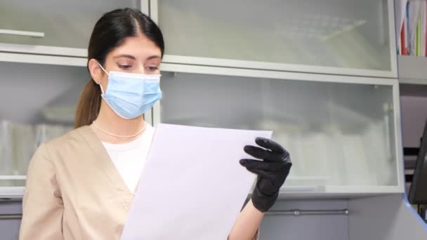 マスクの女性歯科医は オフィスに立ちながら患者のX線画像を見ている 現代の歯科医 女性歯科医 — ストック動画