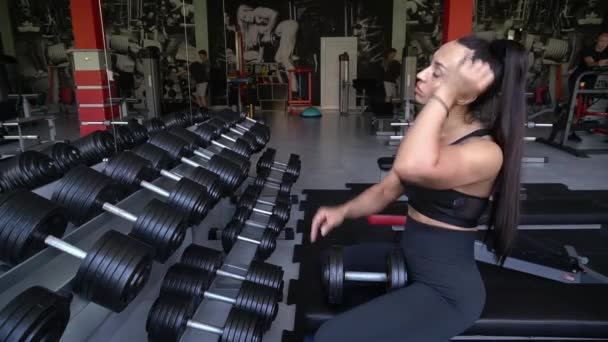 Brunette Works Out Gym She Lifts Dumbbells While Sitting Front — Vídeos de Stock