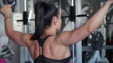 Active, fit woman trains her back and arms in the gym. Female powerlifter close-up while training in a modern gym studio. 4k video