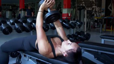Female athlete doing bench press workout with dumbbell in fitness gym.