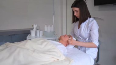 A cosmetologist massages a womans face, that lies on the shelf in an elite beauty salon. Proper facial care. Prevention of skin aging. Antiaging massage