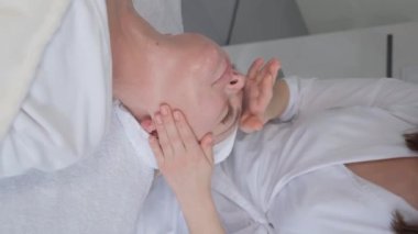 Vertical video. A beautician pleasantly massages a womans face. Anti-aging facial massage. 