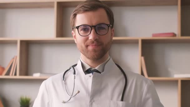 一个穿着白色制服 眼镜站在书架上的英俊年轻医生的画像 临床医生的画像 — 图库视频影像