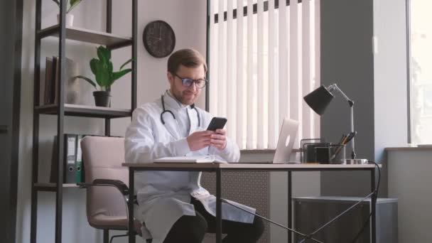 Jovem Médico Profissional Sentado Mesa Escritório Olhando Para Smartphone Médicos — Vídeo de Stock