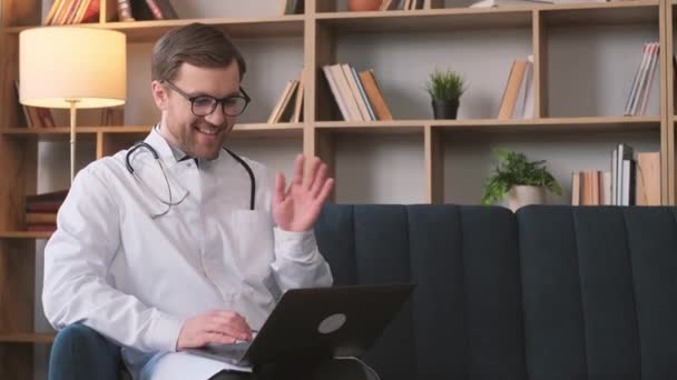 一位身穿白色制服 戴着眼镜 留着胡子的积极医生坐在病房里 与网上的某个人交谈 年轻医学专家 — 图库视频影像
