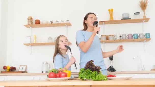 妈妈和女儿在家里的厨房里用勺子唱歌 一家人在厨房里快乐地一起做饭 — 图库视频影像