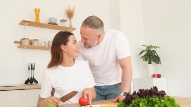 一位年轻女子正在切蔬菜 准备健康的沙拉 而她的丈夫则在厨房拥抱她 — 图库视频影像