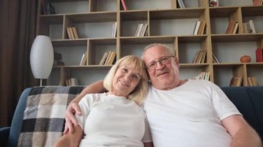  Gözlüklü, sevgi dolu yaşlı bir adam gülümseyen karısına sarılıyor ve kameraya bakıyor. Gri saçlı adam ve kadın aile videosu için poz veriyor..