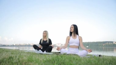 Young women practicing meditation in the morning in a bright sunny park outside the city. Meditation in the lotus position. Practicing yoga