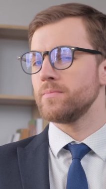 Portrait of an office worker wearing glasses, he is looking at the camera and smiling. Work of a manager in the office. Businessmen. Vertical video