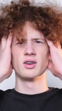 Close-up of face of worried red-haired curly guy looking at camera. Headache. Poblem. Fail. Trouble. Vertical video