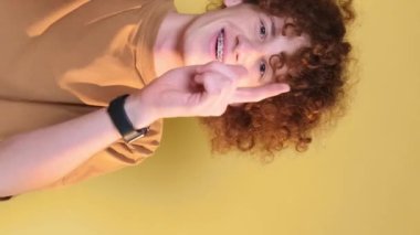 A cheerful, playful young man with a chic hairstyle shows positive emotions to the camera. Hand gestures. A student on a brown background. Vertical video