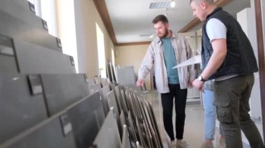 Satıcıyla birlikte genç bir çift yer tamiri için büyük bir seramik fayans seçiyor. İnşaat süpermarketinde tamir malzemelerinin aile seçimi.