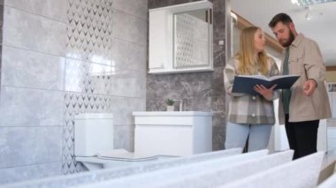 Profesyonel bir inşaat salonunda genç bir aile. Bir çift banyo mobilyalarını katalogdan seçiyor..