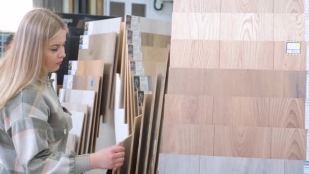 一位年轻貌美的女士正在一家大型五金店里选择地板覆盖物 木地板样品 层压板 — 图库视频影像