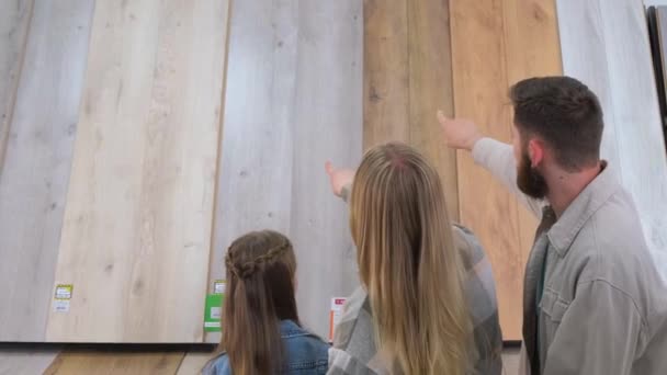 一个有孩子的年轻家庭在一家大的五金店里选择一个铺着地板的地方 为新房子选择建筑材料 木地板样本 — 图库视频影像