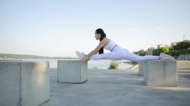 Açık havada bacak esneme egzersizi yapan zinde bir esmer. Çekici bir kız sicimin üzerinde oturuyor. Spor yaşam tarzı..