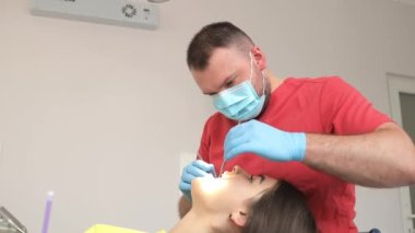 Güzel genç bir kadın dişçi muayenehanesinde diş tedavisi görüyor. Dişçi hastaların dişlerini tedavi eder..