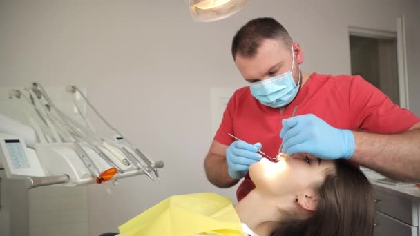 歯科医は 口鏡と歯科掘削機で患者の歯を調べています ハンサムな若い歯科医は美しい女性の歯を治療しています — ストック動画