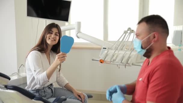 女性は 歯医者のオフィスの検査の後 鏡と笑顔を見ます 歯科クリニックで若い美しい患者 — ストック動画