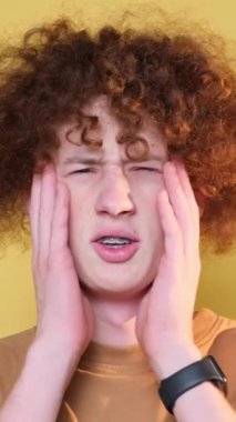 Kahverengi arka planda duran genç bir adamın kameraya poz vermesinin başarısızlığı. Kızıl saçlı kıvırcık adam olumsuz duygular gösteriyor. Başarısız. Üzüntü.