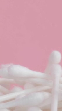 Pembe arka planda pamuklu çubuklar, plastik pamuklu bezler. Dikey video.