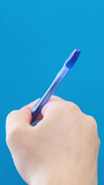 青い背景に短いストロークでボールペンで手を書く男性 バーティカルビデオ — ストック動画